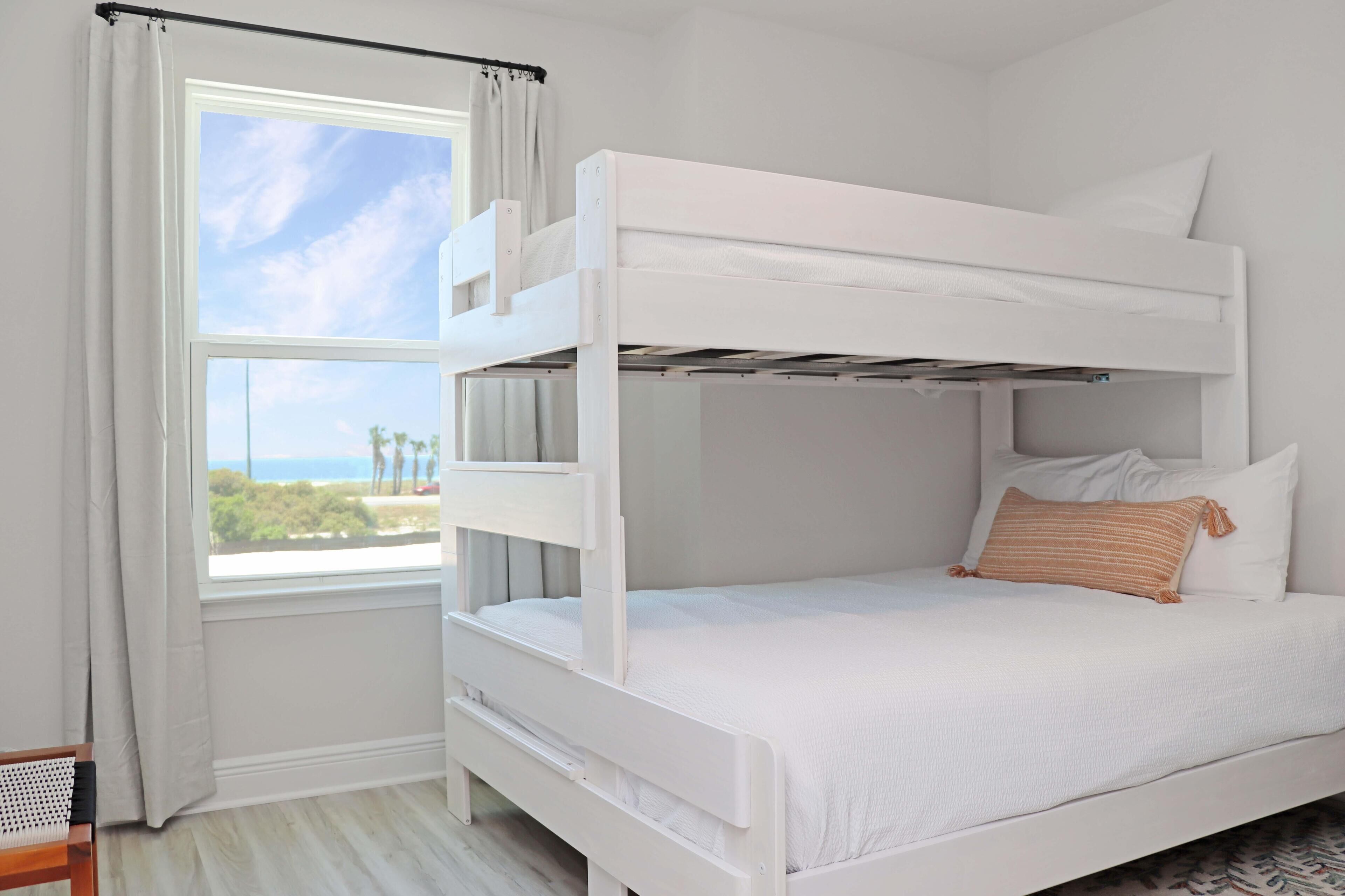 Une chambre avec un lit superposé, une fenêtre, des rideaux et une vue sur l’extérieur.