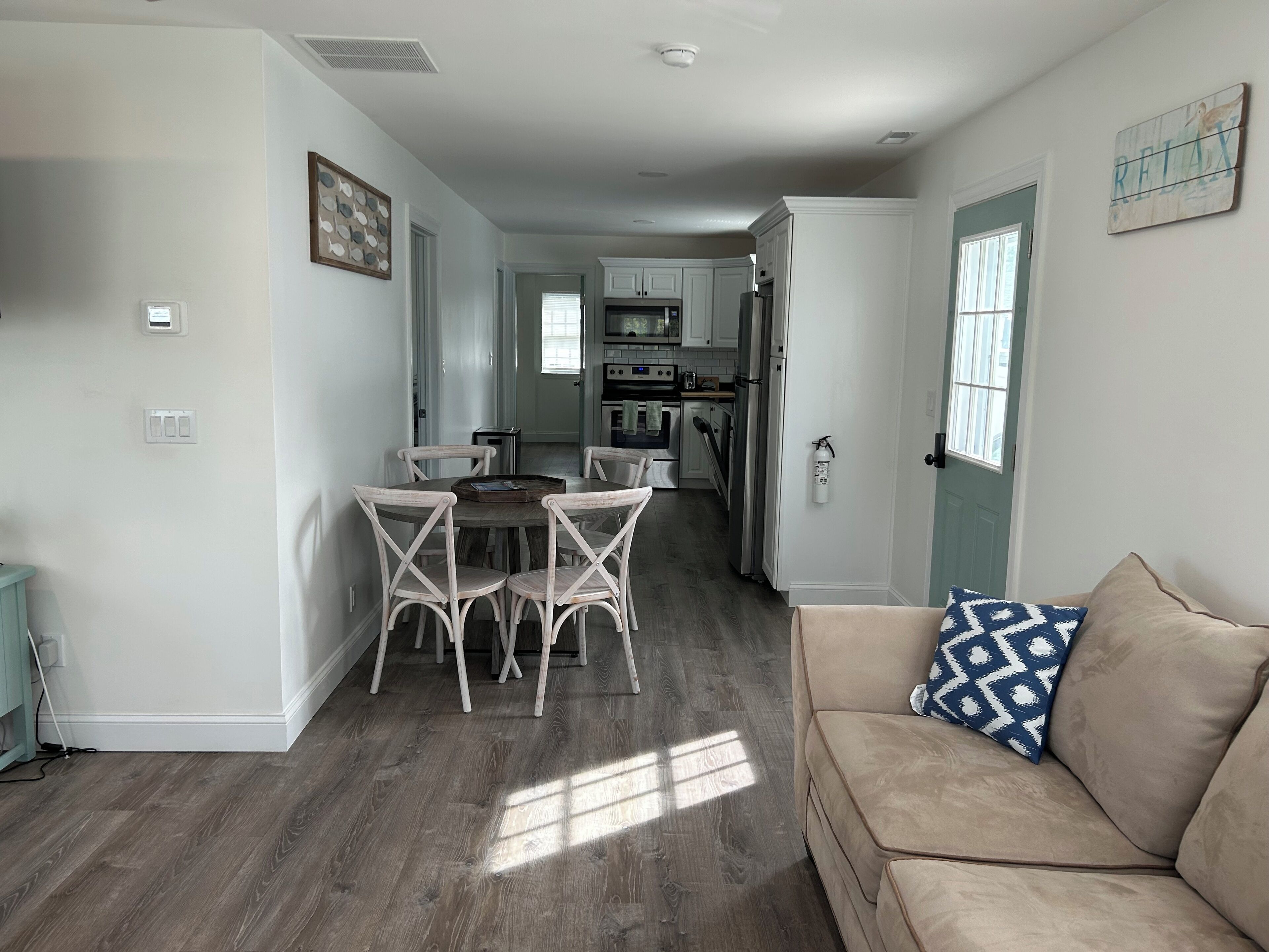 A modern kitchen with white cabinets, a dining area with a round table and four chairs, and a beige sofa with a patterned pillow.