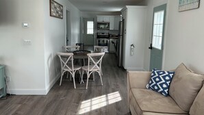 A modern kitchen with white cabinets, a dining area with a round table and four chairs, and a beige sofa with a patterned pillow.