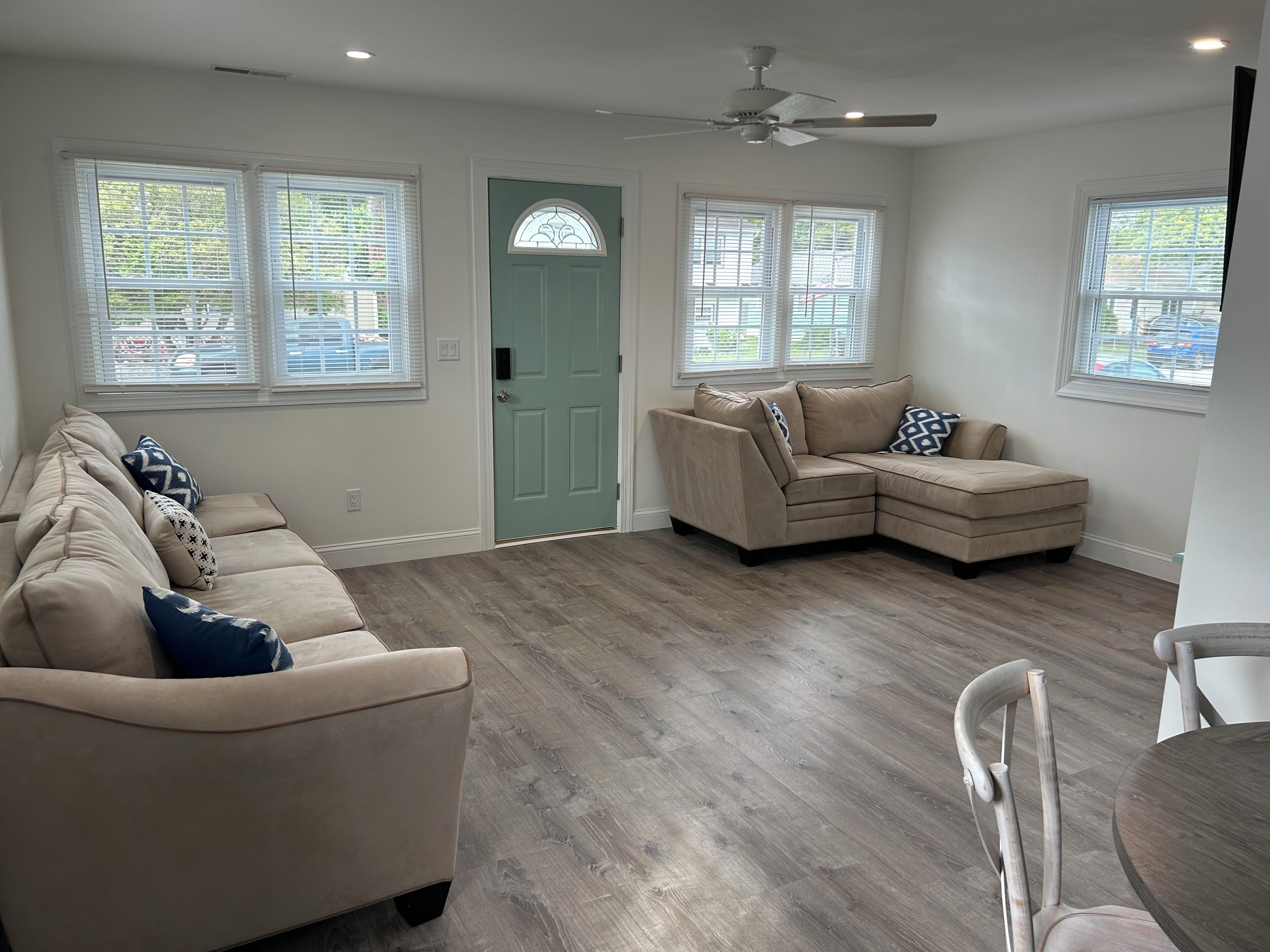 A spacious living room with a beige sectional sofa, a dining table with chairs, and a ceiling fan.