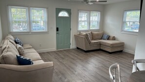 A spacious living room with a beige sectional sofa, a dining table with chairs, and a ceiling fan.