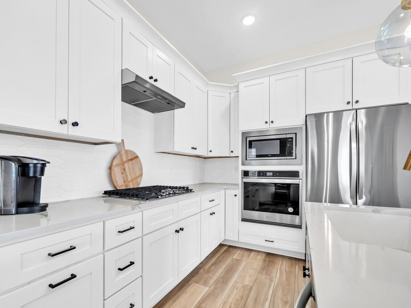 A modern kitchen with white cabinets, a stainless steel refrigerator, a microwave, and an oven.