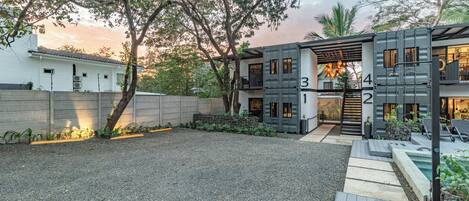 A modern two-story building with a gravel driveway and a small pool area.