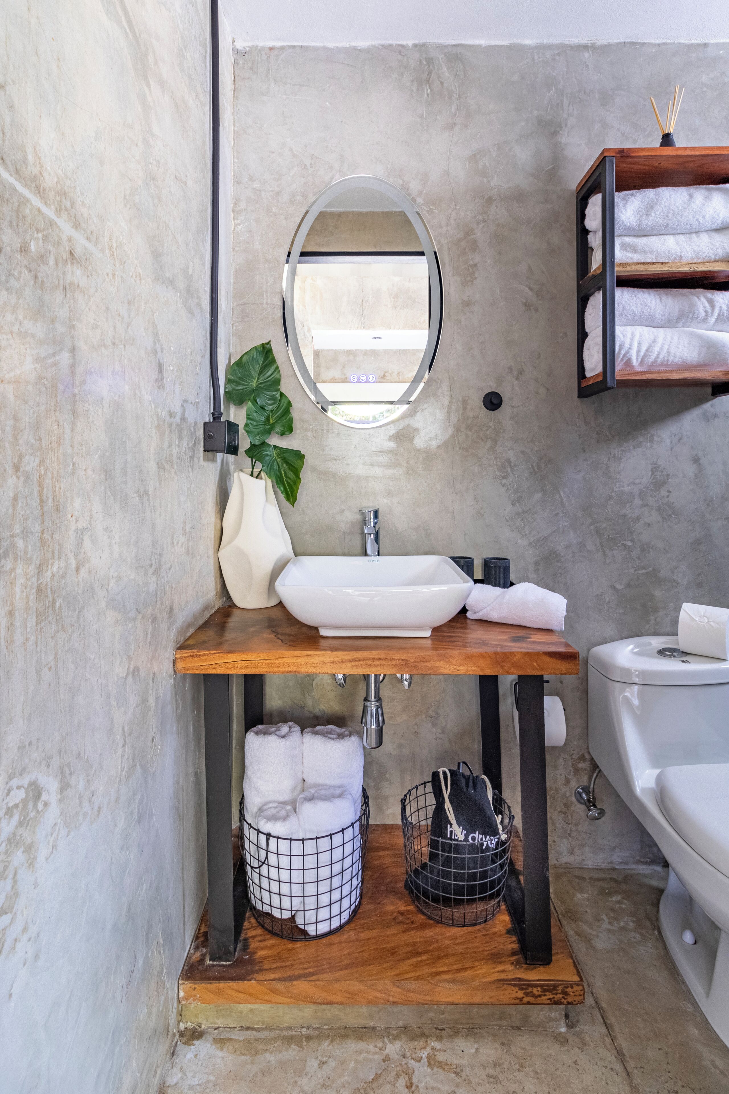 A bathroom with a wooden vanity, white sink, and a round mirror. There are towels and a black bag on the vanity.