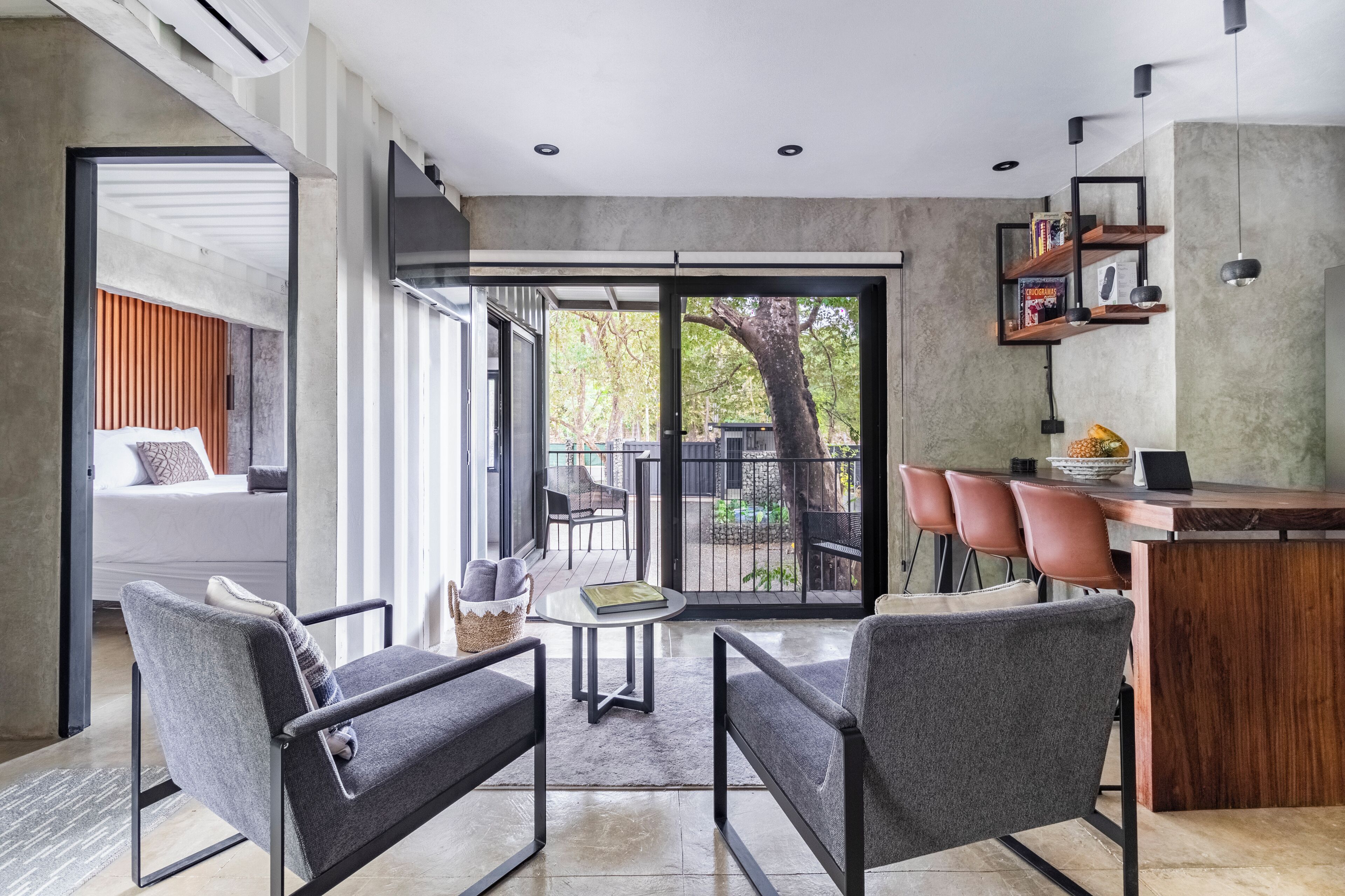 Una cocina moderna con encimera de madera, una zona de comedor con sillas tapizadas en gris y un amplio ventanal corredero que da a un patio exterior.