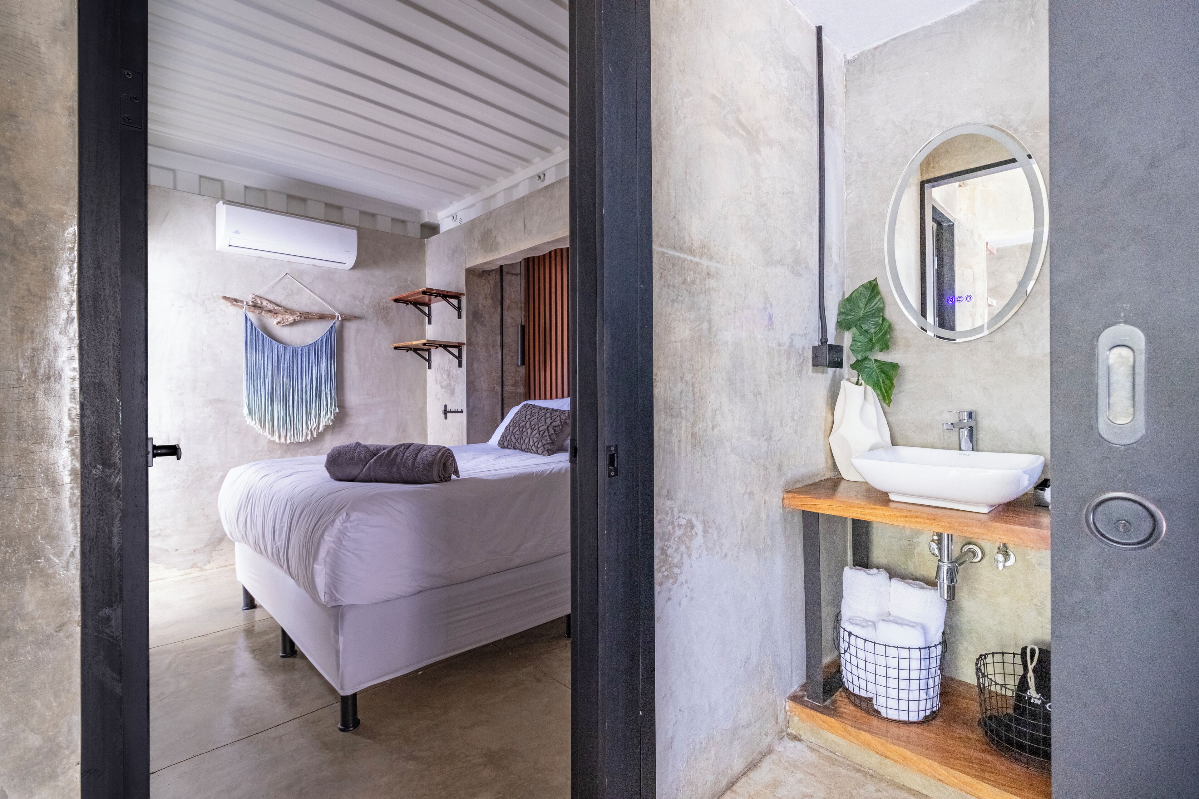 A modern bedroom with a bed, hanging towel, and a bathroom with a sink and mirror.