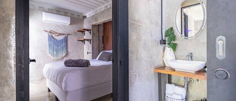 A modern bedroom with a bed, hanging towel, and a bathroom with a sink and mirror.