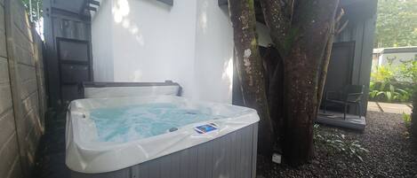 A hot tub next to a tree in a garden area with a white wall and a door in the background.