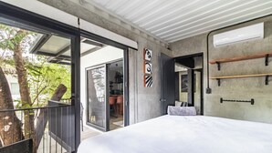 A modern bedroom with a large bed, sliding glass doors to a balcony, and a concrete wall with minimalist decor. - Z102 studios (Potrero)
