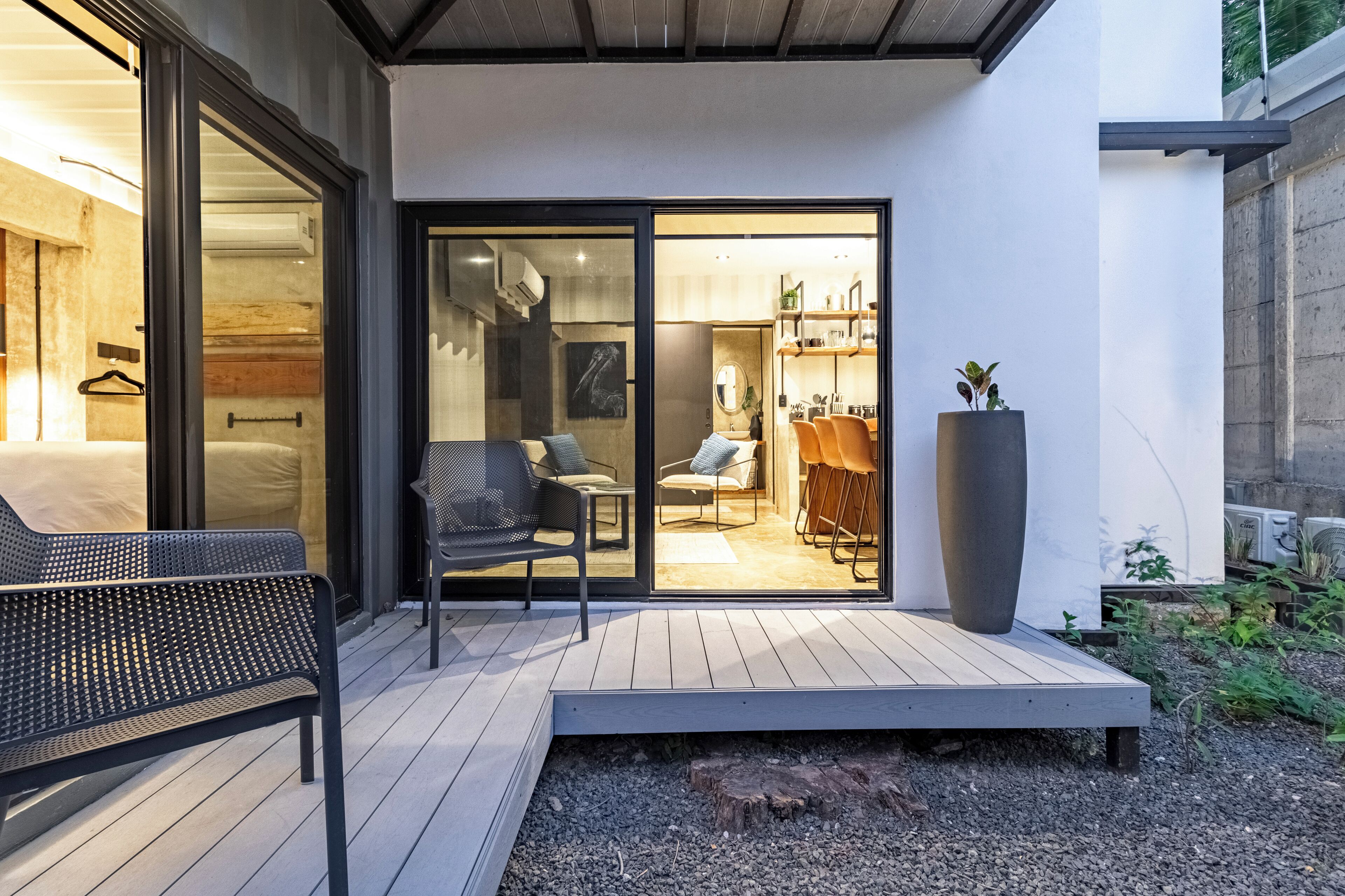 A modern outdoor patio with a wooden deck, a metal bench, and a large planter.