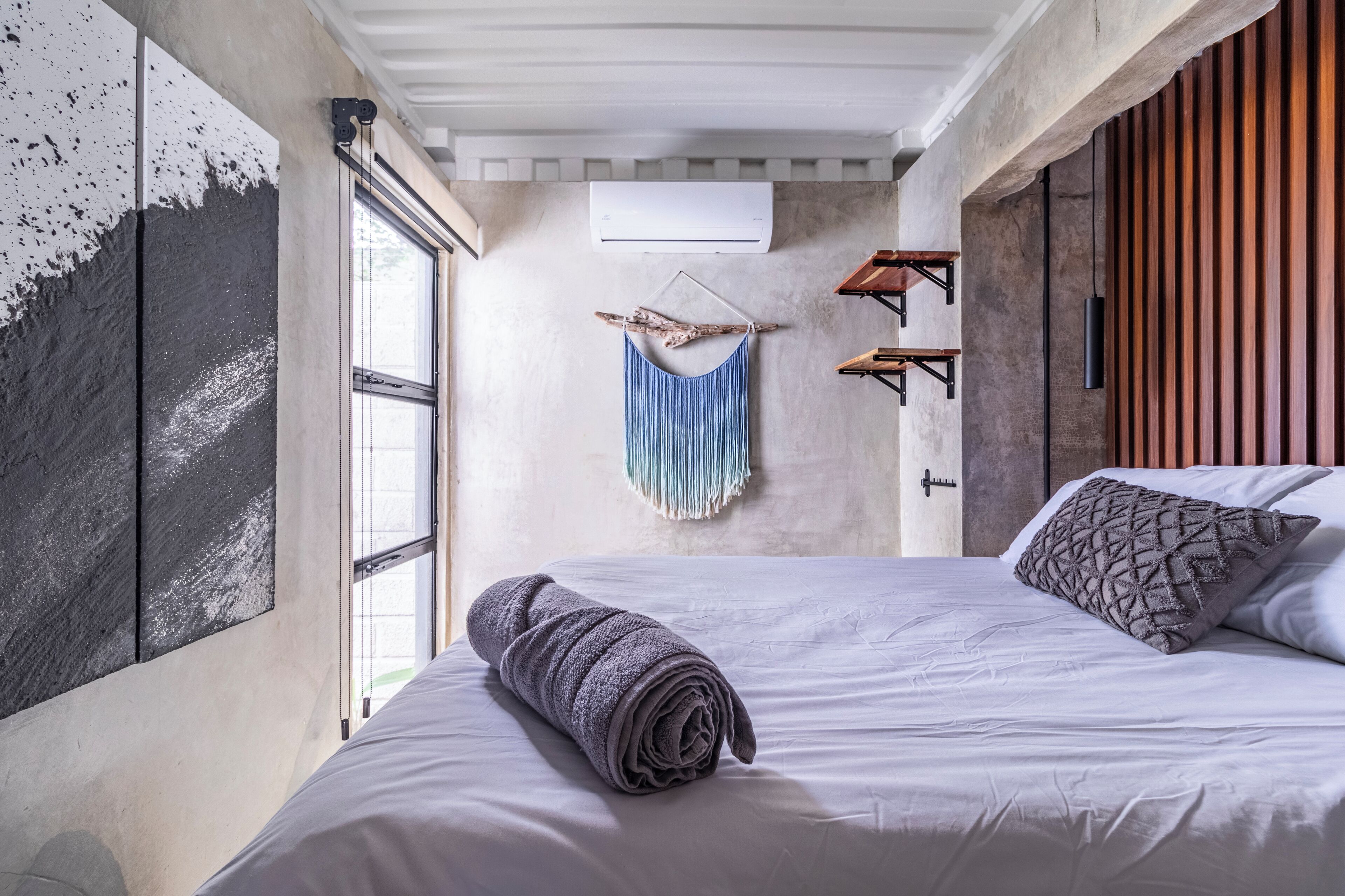 Un dormitorio moderno con una cama grande, un adorno colgante de macramé y un revestimiento de pared de listones de madera.
