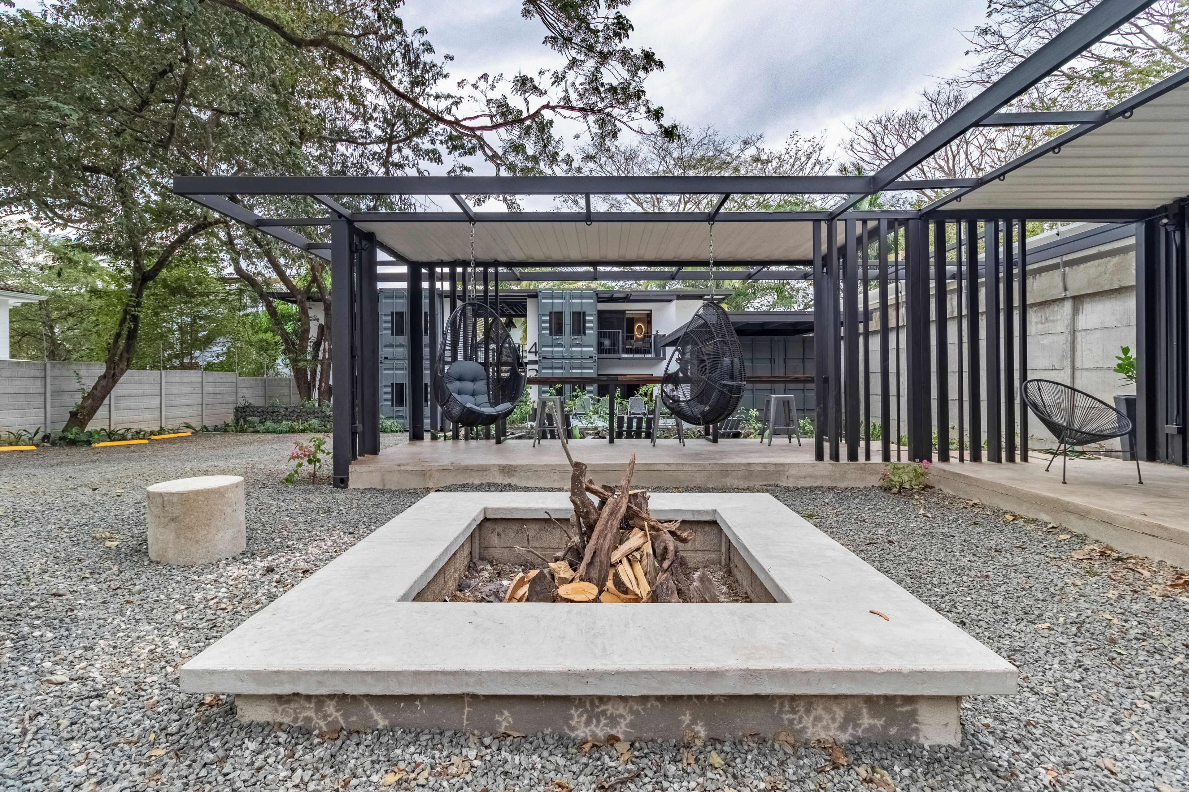 Un patio moderno al aire libre con un hogar para fuego, zona de estar y una estructura de pérgola.