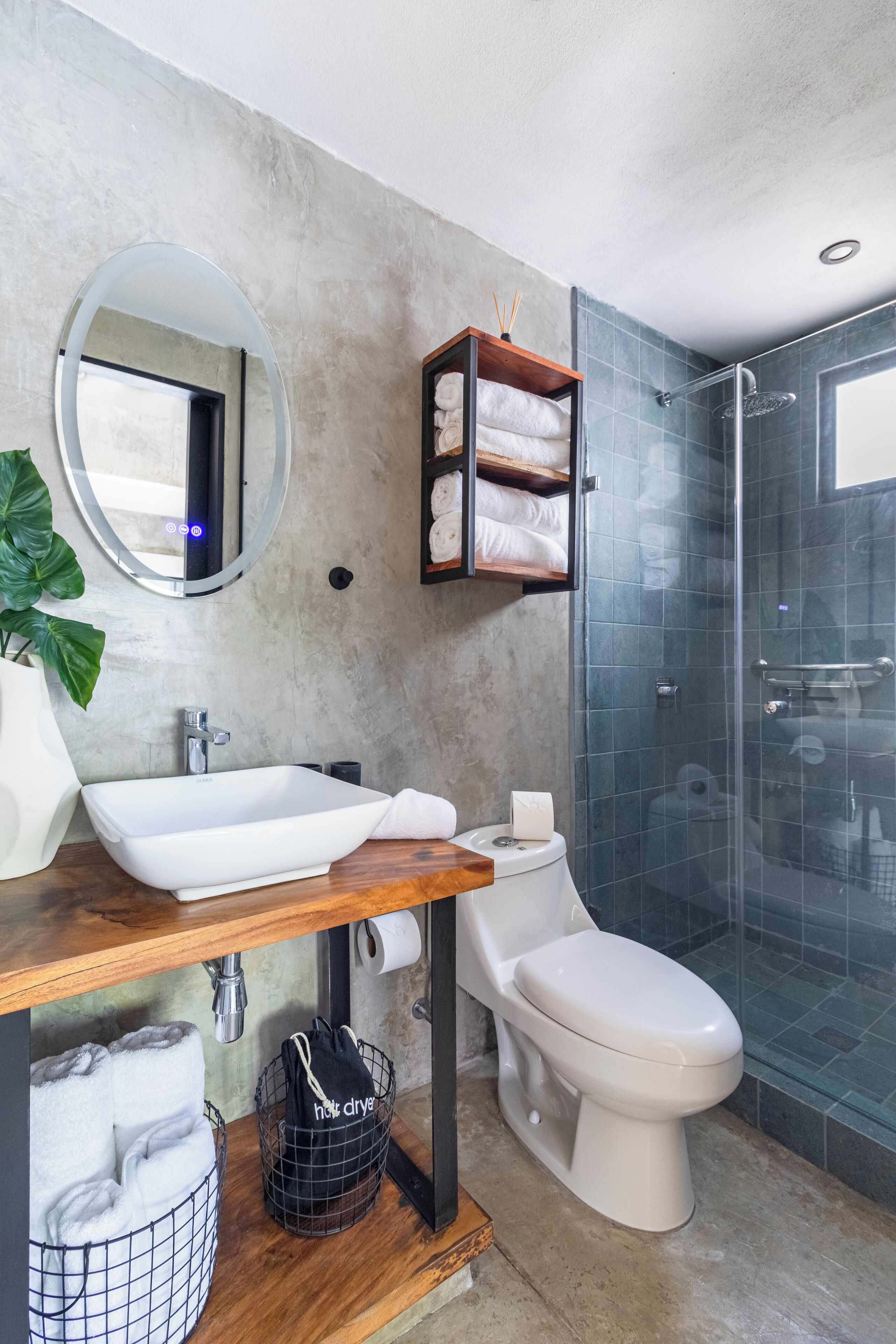 A modern bathroom with a rectangular sink, a toilet, a glass shower enclosure, a round mirror, and a towel rack.