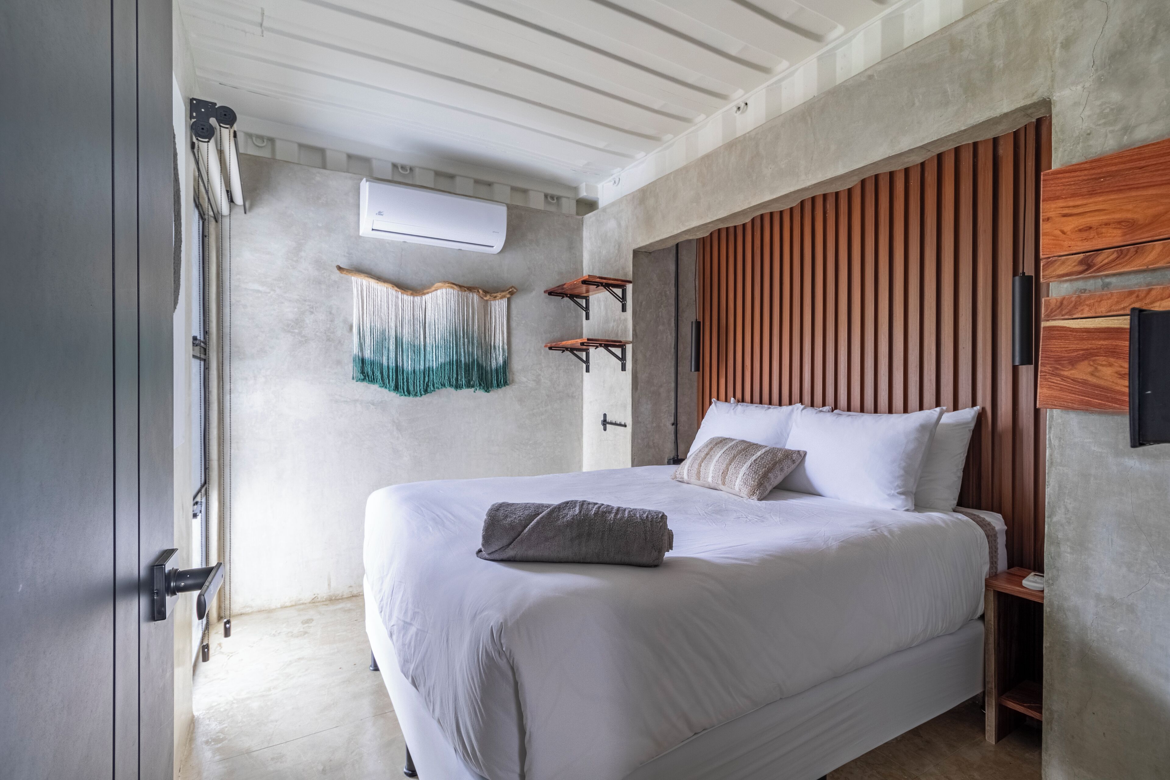 Un dormitorio con una cama grande, cabecero de madera y una pared de concreto decorativa.