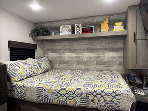 A bedroom with a bed, a headboard, a shelf with decorations, and a wooden wall.