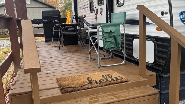 Een overdekt terras met een houten trap naar een camper.