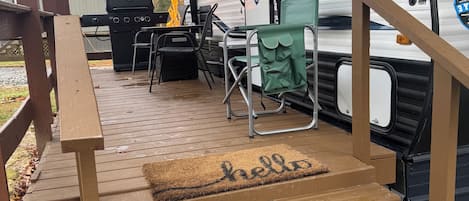 A covered deck area with a wooden staircase leading to a camper.