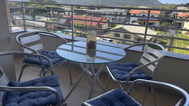 Un balcon avec une table en verre, des chaises en métal et une vue sur les immeubles et les montagnes.
