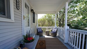 Eine Veranda mit weißer Reling, einer Fußmatte und zwei Korbstühlen mit blau-weißen Kissen.