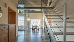 A modern interior with a wooden cabinet, a staircase with metal railings, and a view of mountains through large windows.