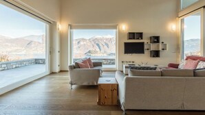 A spacious living room with a large window offering a mountain view, a flat-screen TV mounted on the wall, and a cozy seating area with a sofa and chairs.