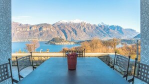 A table with chairs and a vase, overlooking a mountainous landscape with a lake and buildings.