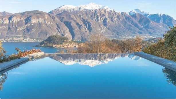 A serene infinity pool with a clear view of mountains and a lake.