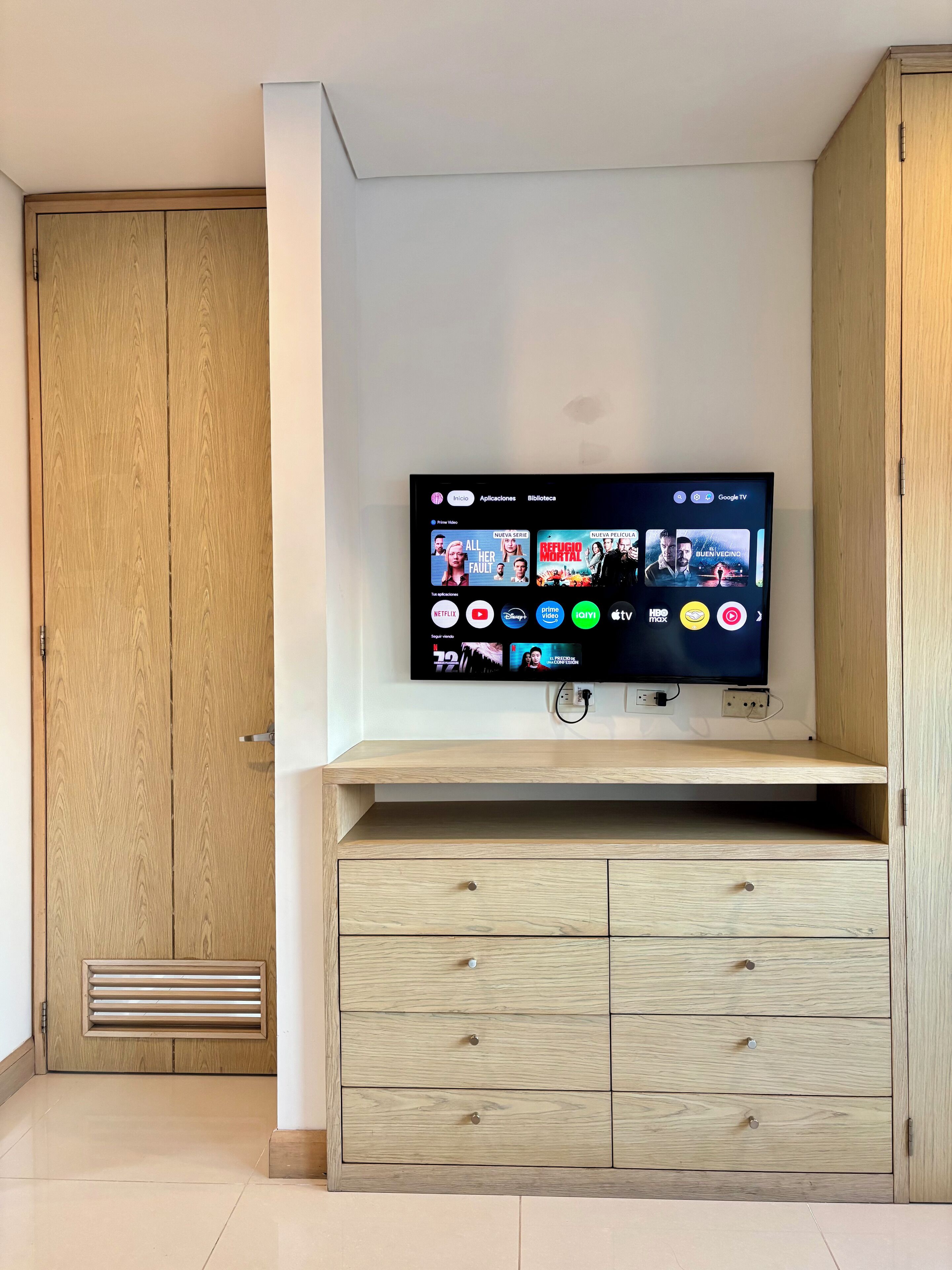 A television mounted on a wooden cabinet with a digital interface displaying various streaming services.