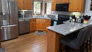 A modern kitchen with wooden cabinets, stainless steel appliances, granite countertops, and a bar area with stools.