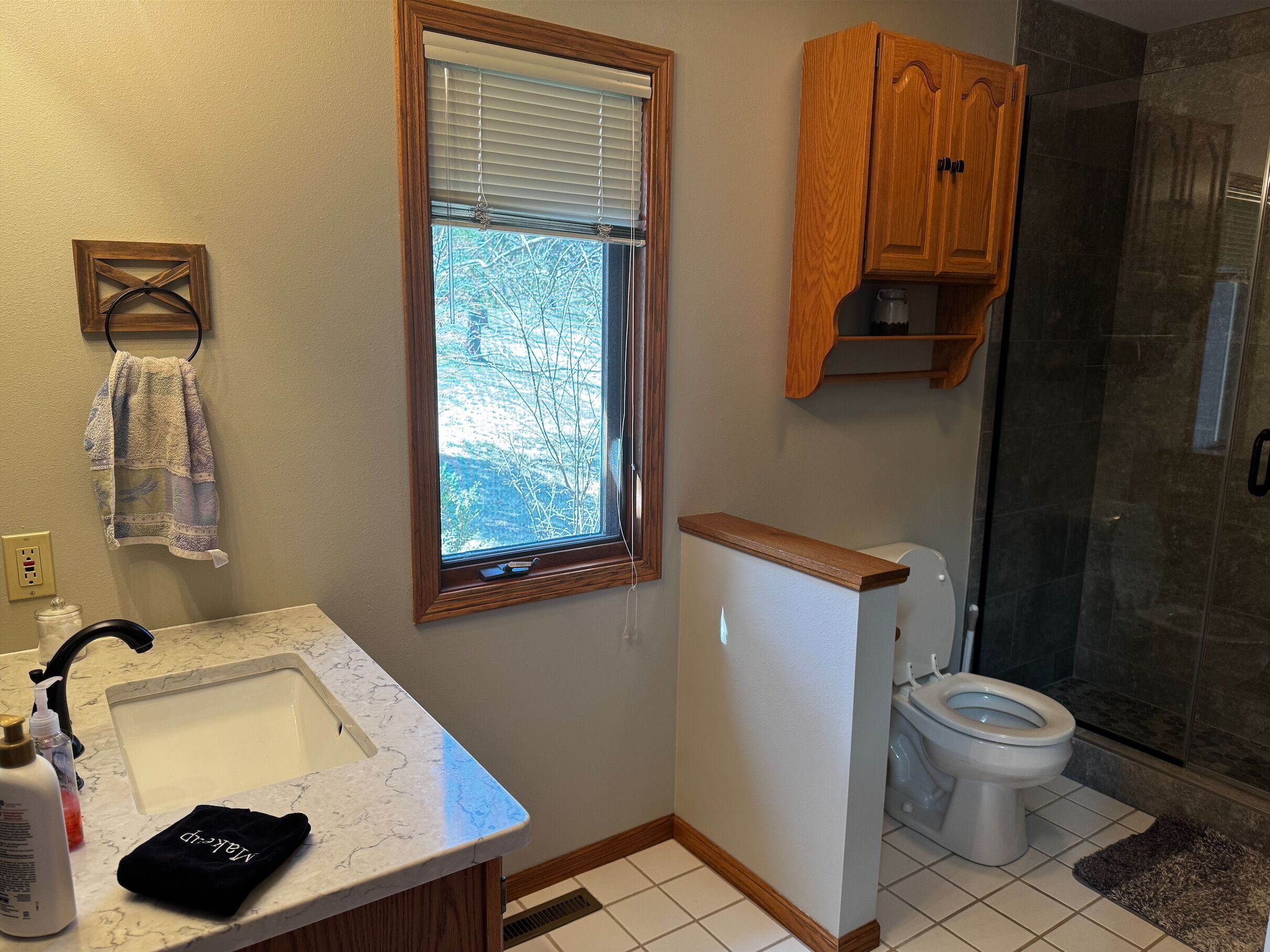A bathroom with a marble sink, wooden cabinet, and a toilet.