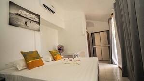 Quarto de hotel com cama, almofadas, um ventilador, um quadro e vista para o exterior.