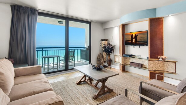 A modern living room with a large sliding glass door leading to a balcony, a flat-screen TV mounted on the wall, and a cozy seating area with a sofa and armchairs. - Sundestin 711 (Destin)