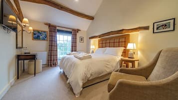 A bedroom with a large bed, a chair, a bedside table, a lamp, and a window with curtains.