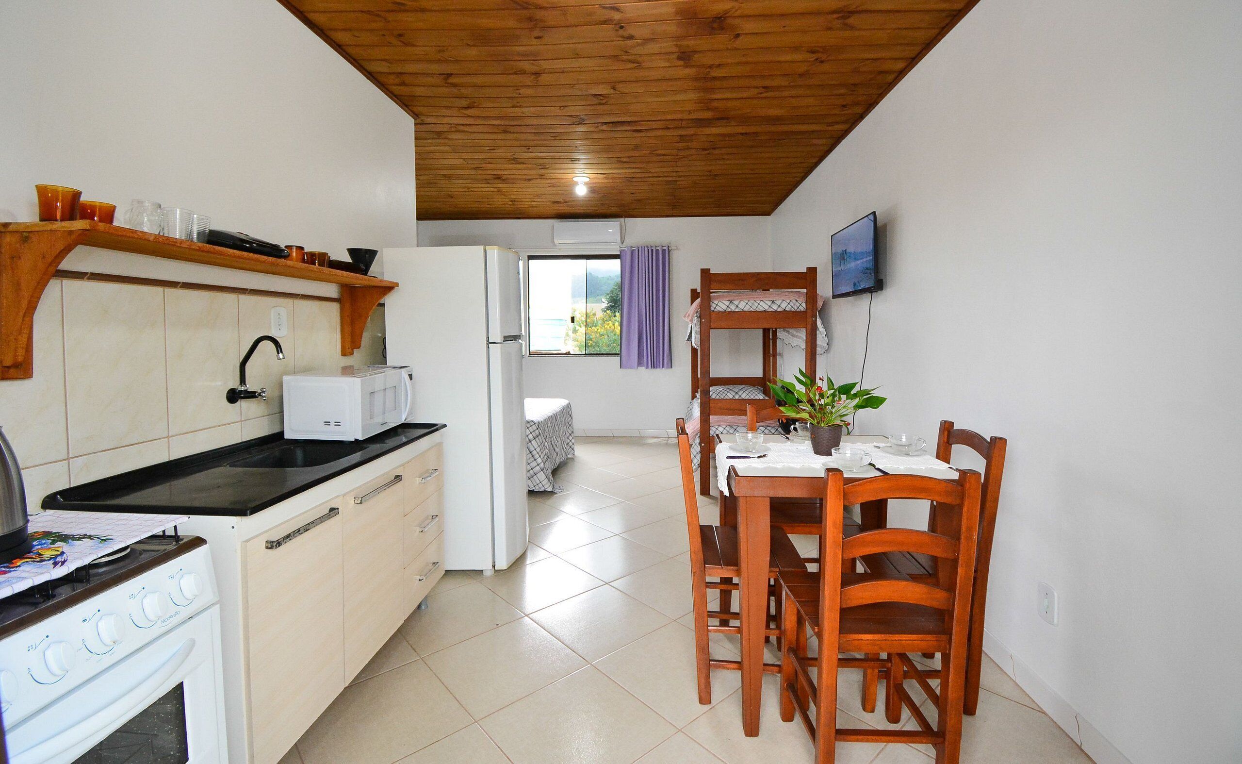 Uma cozinha compacta com fogão, micro-ondas e um espaço de jantar com cadeiras de madeira e uma mesa.