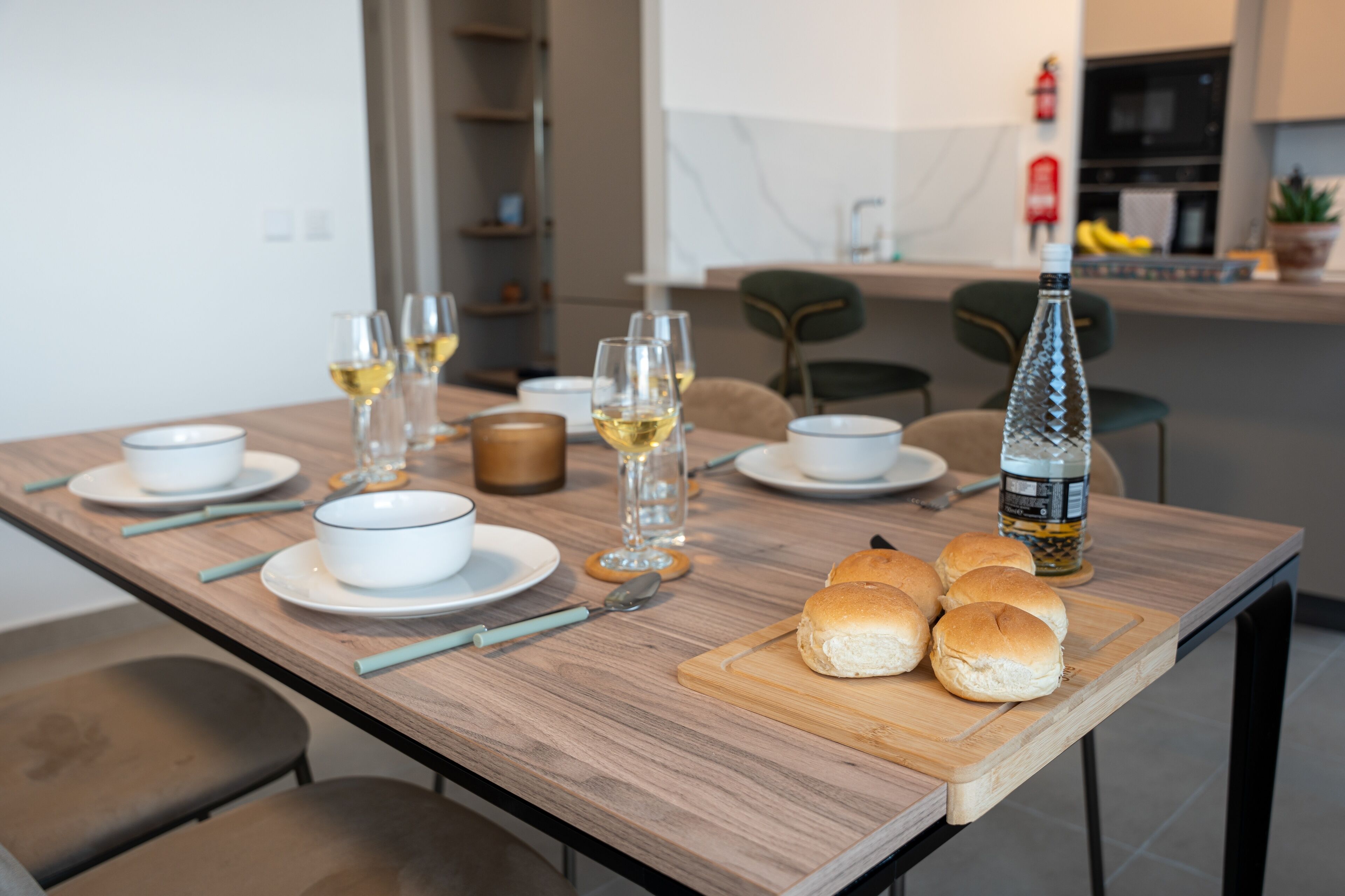 A dining table set with white bowls, wine glasses, and a bottle of olive oil.