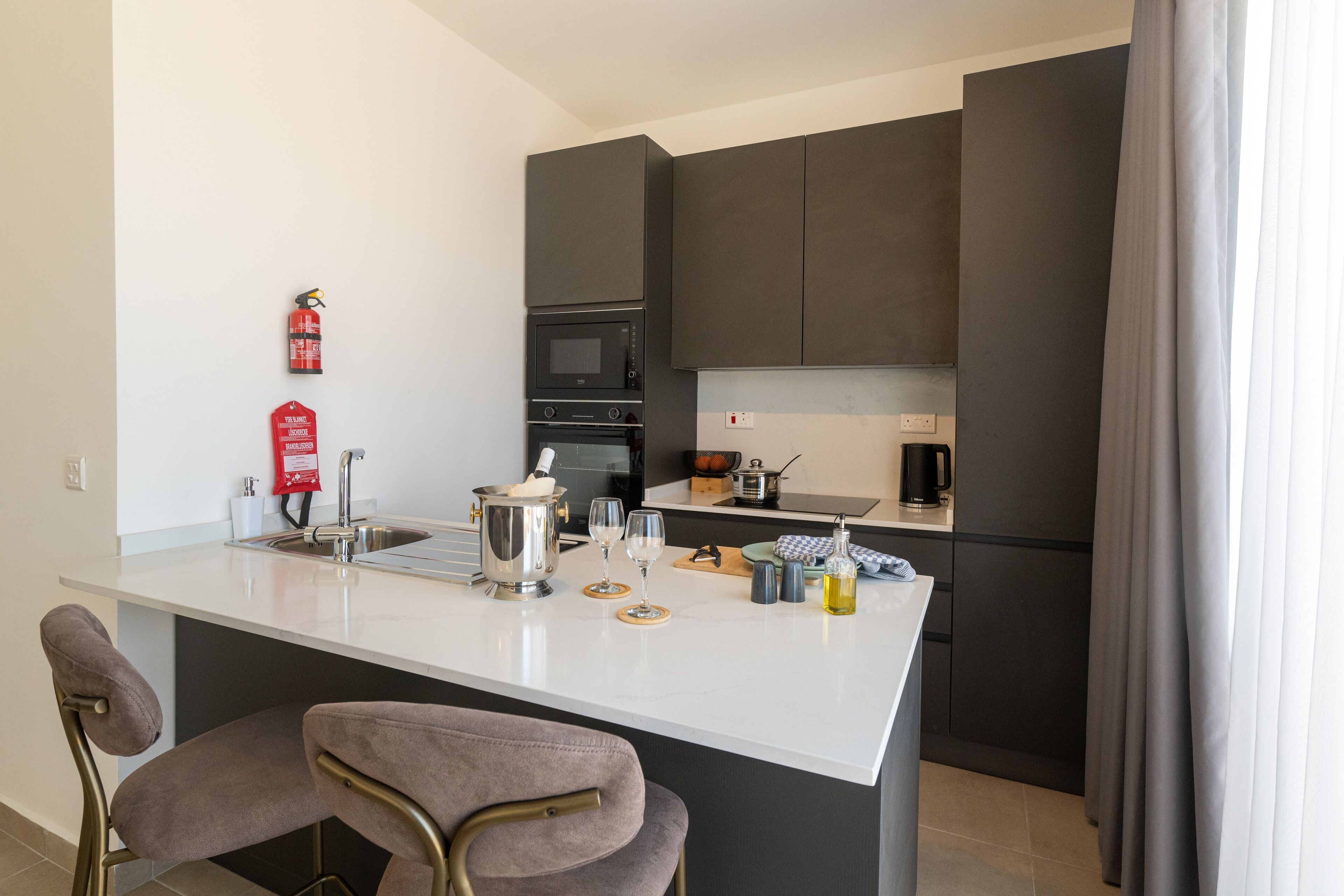 A modern kitchen with a central island, dark cabinets, a microwave, oven, and a coffee maker.