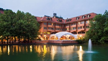 Un hotel con piscina, mobiliario exterior y una fuente.