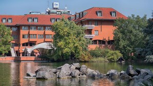 A hotel with red-tiled roofs, multiple balconies, and a water body in front. - Nh Hotel Milano 2 (Segrate)