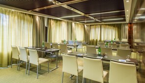Un salón de conferencias con mesas y sillas, cortinas e iluminación en el techo.