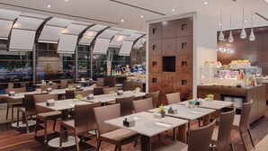 Un restaurante moderno con varias mesas y sillas, una vitrina de vidrio con productos alimenticios y un ventanal que ofrece vistas de la ciudad.