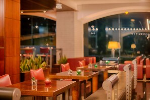 Un restaurante con mesas de madera, sillas rojas, ventanas amplias y luces colgantes.