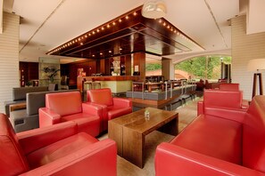 Un hallo amplio con asientos de cuero rojo, una mesa de centro de madera y un área de bar con vistas a zonas verdes.