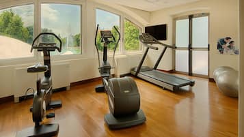 Ein Fitnessstudio mit Trainingsgeräten, großen Fenstern und einem Laufband.