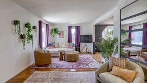 A modern living room with a sofa, armchairs, a coffee table, and a TV. There are plants on the walls and a large mirror. - New 5BD Near UNL & DT - Poker Table & Games (Lincoln)