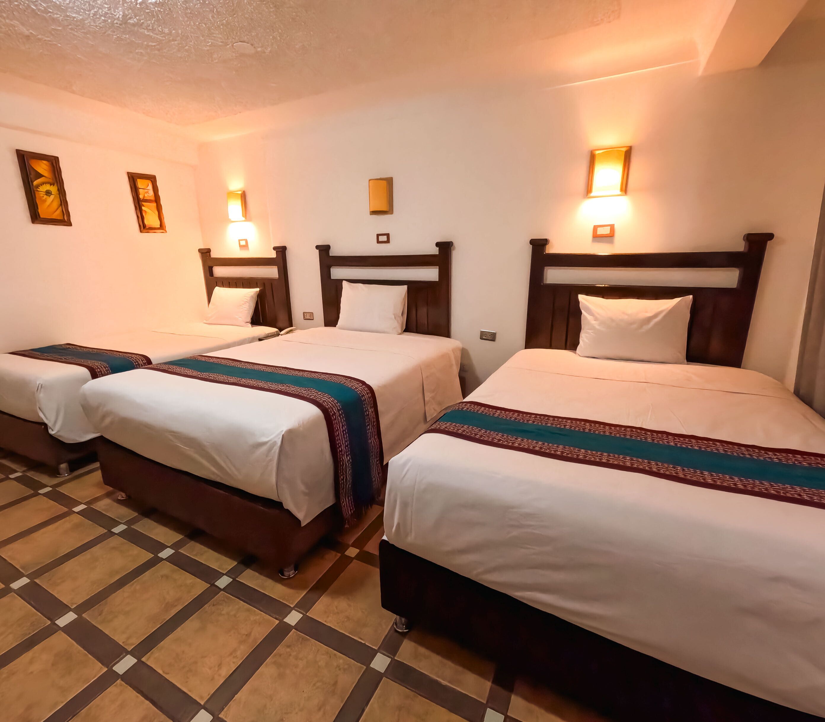 A hotel room with three single beds, each with a wooden headboard and a patterned bedspread.