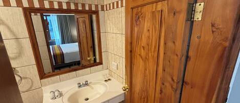 A bathroom with a wooden door, a white sink, and a mirror.