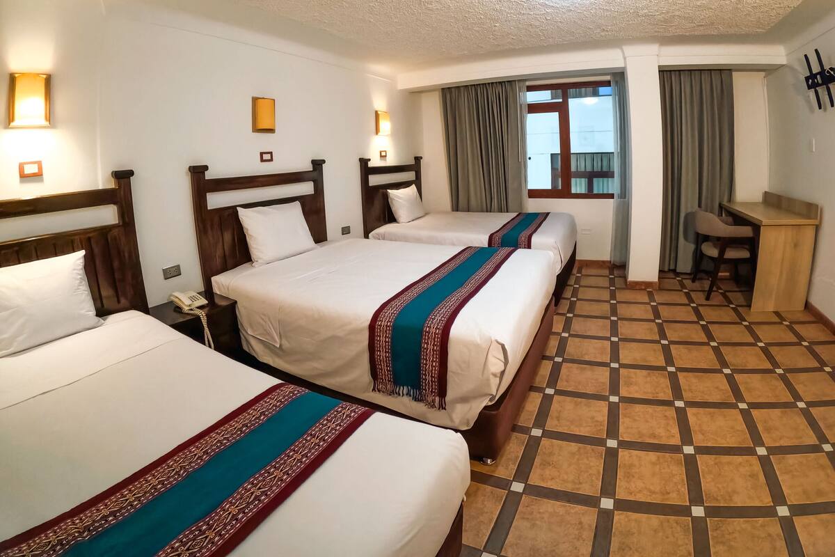 A hotel room with three beds, a desk, and a window with curtains.