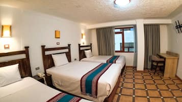 A hotel room with three beds, a desk, and a window with curtains.