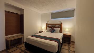 Una habitación de hotel con cama, lámparas de noche, un banco y una lámpara de techo.