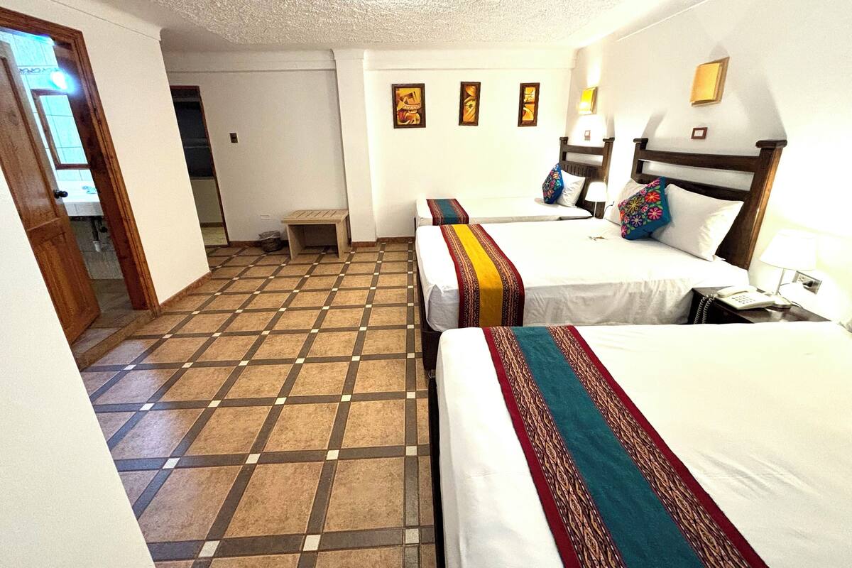A hotel room with two beds, a small table, a chair, and a bathroom visible through an open door.